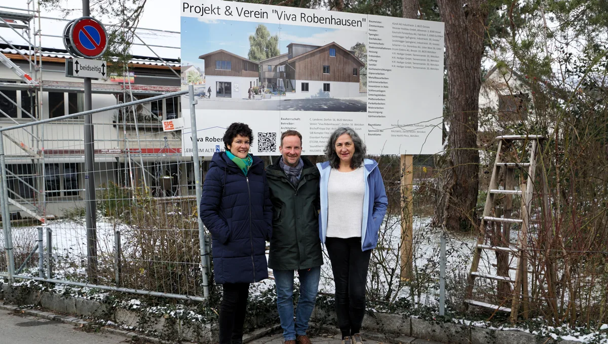 Man sieht drei Personen vor einer Info-Tafel einer Baustelle.